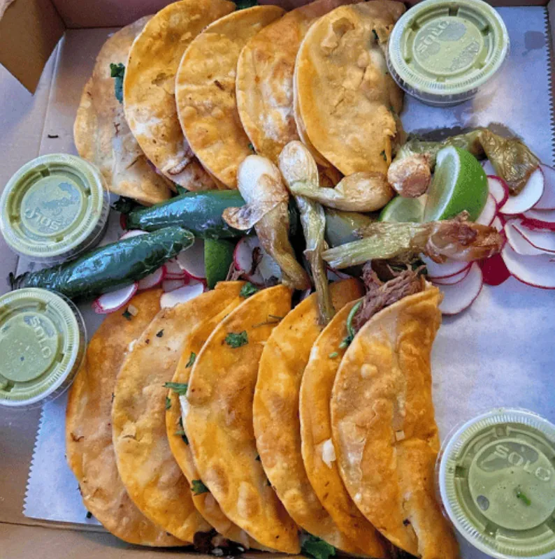 A family tray of birria tacos with consomé and salsas